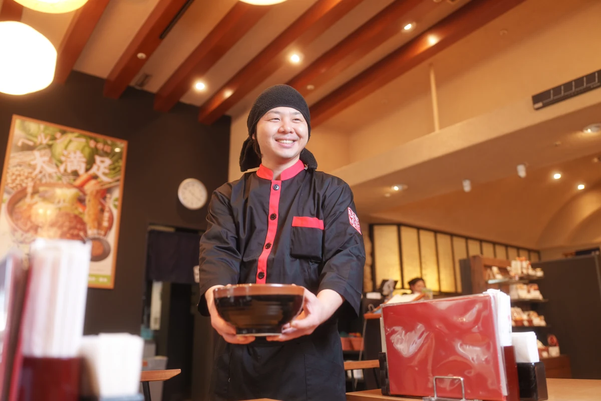 らーめんを手に笑顔で接客する田所商店のスタッフ